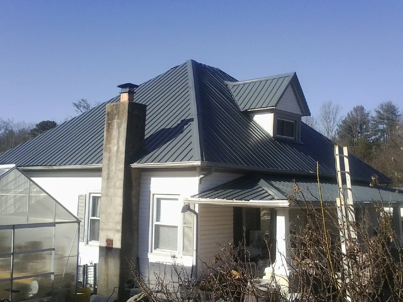 Dark blue standing seam metal roof on a white farmhouse with dormer — Slate & Tile Roof Repair by Roofing Brothers in Oskaloosa