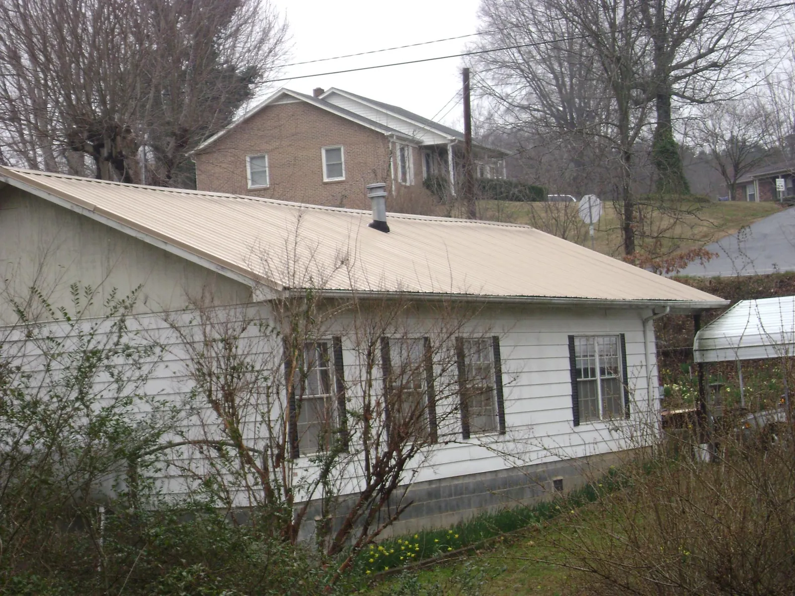 Tan metal roof on a white sided house set into a hillside — Commercial Roofing by Roofing Brothers in Oskaloosa